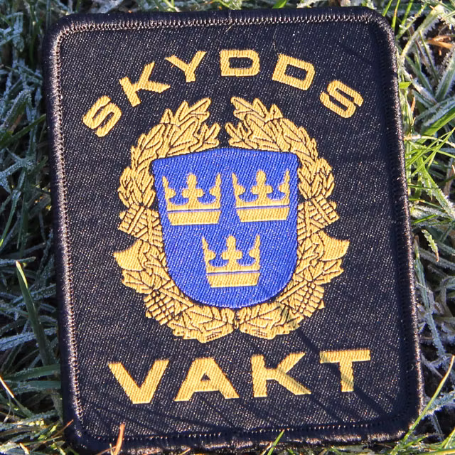 Solstrålar når ett Skyddsvakt tygmärke kardborre Svart under produktfotografering.