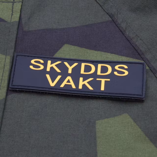 Skyddsvakt PVC Avlång Kardborremärke på en M90 kamouflage jacka.