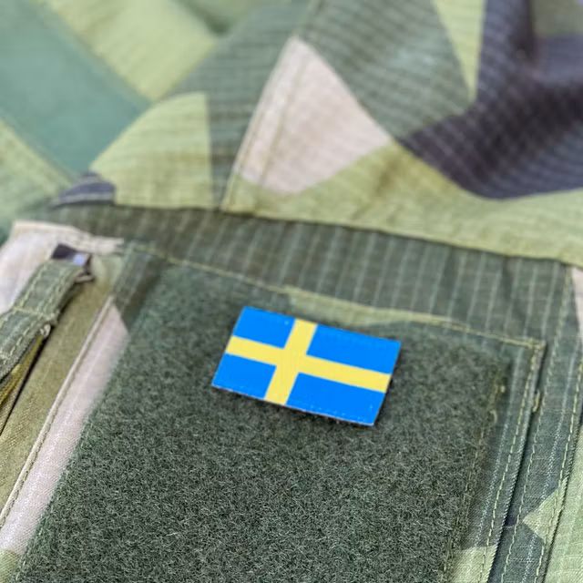 Seen from an angle and mounted on loop fabric is a Sweden Flag Hook Patch Arm