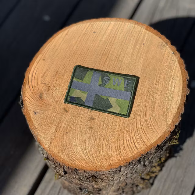 A Sweden Flag OPS M90 Patch from TAC-UP GEAR seen from an angle on a piece of wood