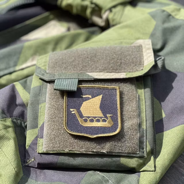 A Viking Ship Shield Large Olive and Black Hook Patch seen from an angle mounted on a NCWR Jacket M90