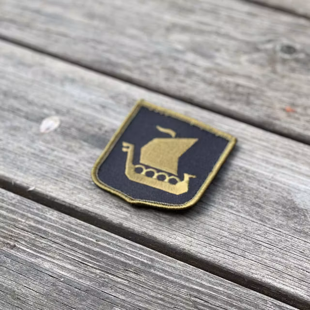 Viking Ship Shield Large Olive and Black Hook Patch seen from an angle lying on wooded floor