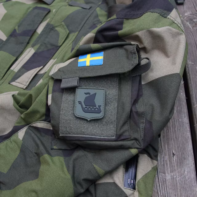 En Svensk flagga och ett Vikingship Shield Hook PVC Green/Black Patch märke på en NCWR Jacket M90.