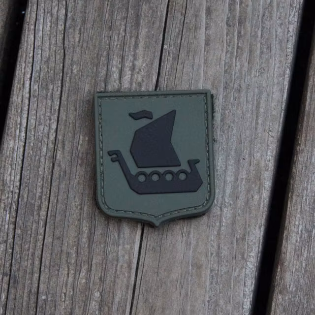 Ett Vikingship Shield Hook PVC Green/Black Patch mot en träbakgrund.