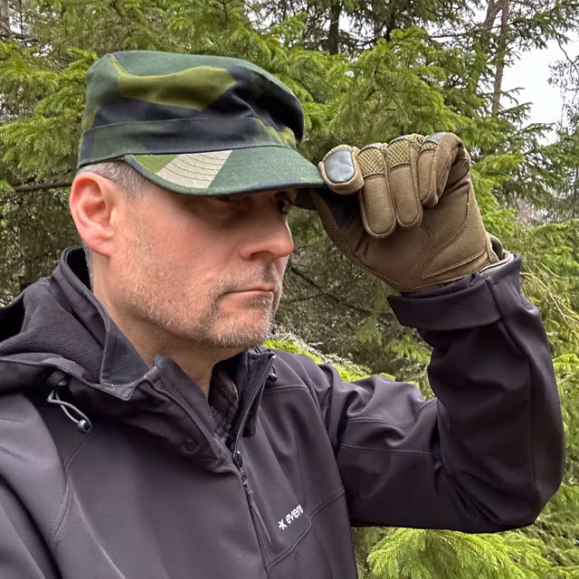 Touching the peak of a Patrol Cap M90 from TAC-UP GEAR on a model in the Swedish forest seen at a slight angle