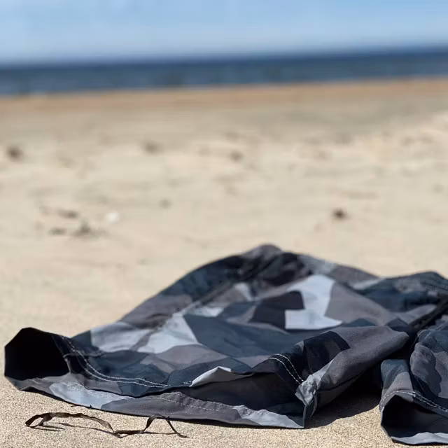 A closer look on a pair of POSEIDON Swim Shorts M90 Grey from TAC-UP GEAR laying on the sand on a beach