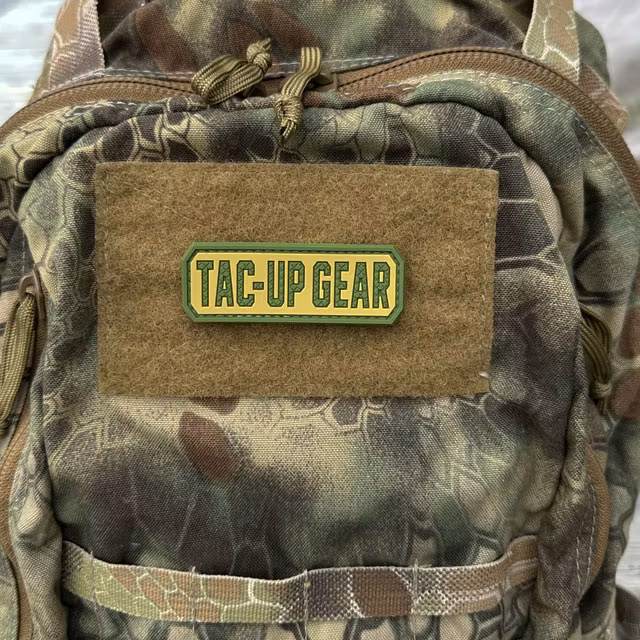 TAC-UP GEAR Multicam Style PVC Hook Patch displayed on a wooden surface