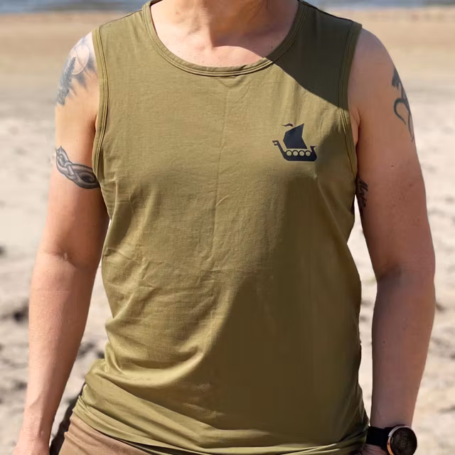 A male model wearing Tank Top Khaki Green from TAC-UP GEAR on a Swedish beach and seen from the front