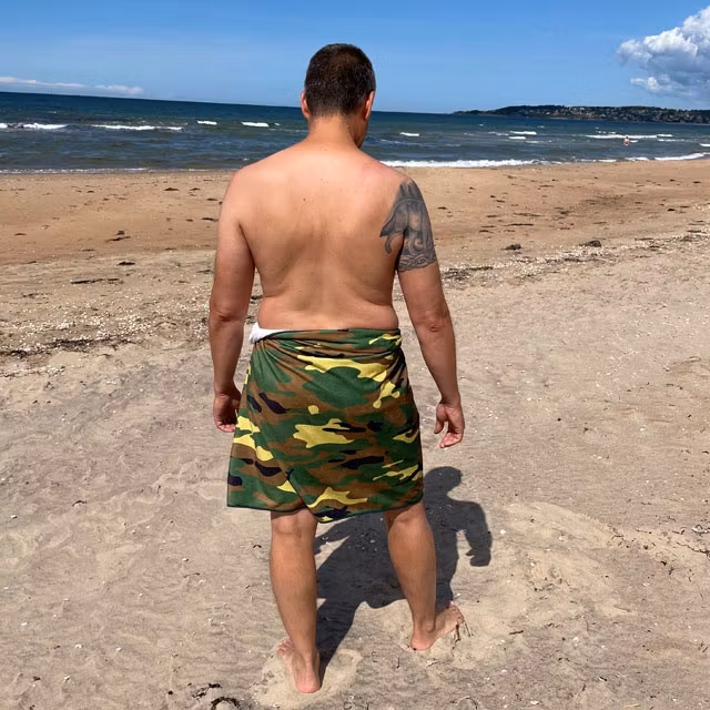Towel Camouflage from TAC-UP GEAR wrapped around models waist on the beach and seen from the back at an angle