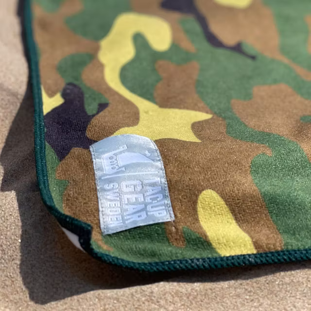 A close up on a Towel Camouflage from TAC-UP GEAR laying in the sun on the beach