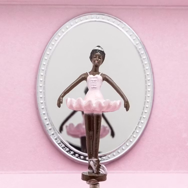 Speldosa med en mörkhyad ballerina, Nia Ballerina. Representation för barn med brun hy.