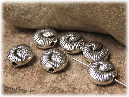 Räfflad fossil snäcka i metall ca 10 mm i diameter