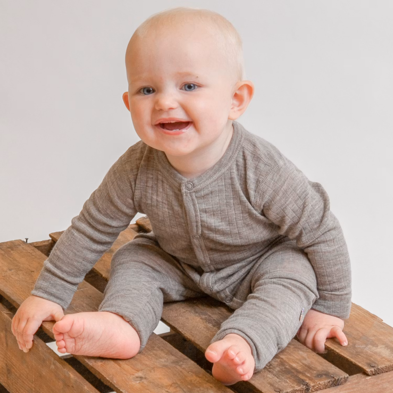 Baby med sesamfärgad ullpyjamas sitter på en låda