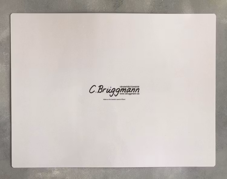 Baksidan på ett praktiskt bordsunderlägg. Den svenska vänsterhänta konstnären C.Brüggmann ligger bakom fårmotivet på framsidan.