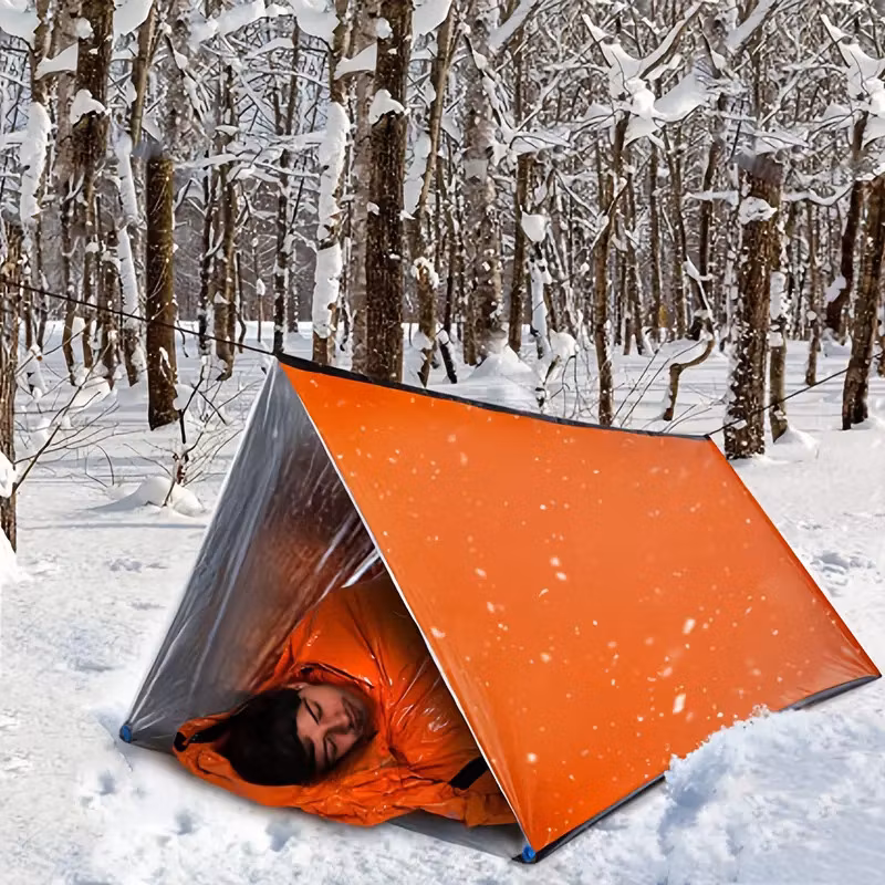 Person som ligger i ett orange nödtält i en snötäckt skog