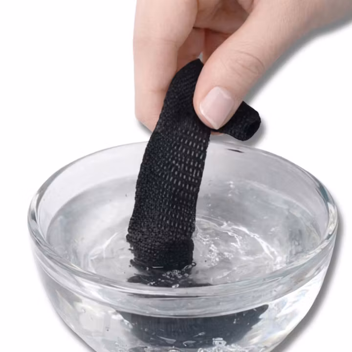 Hand som blöter svart snabbfållband i en glasskål med vatten.