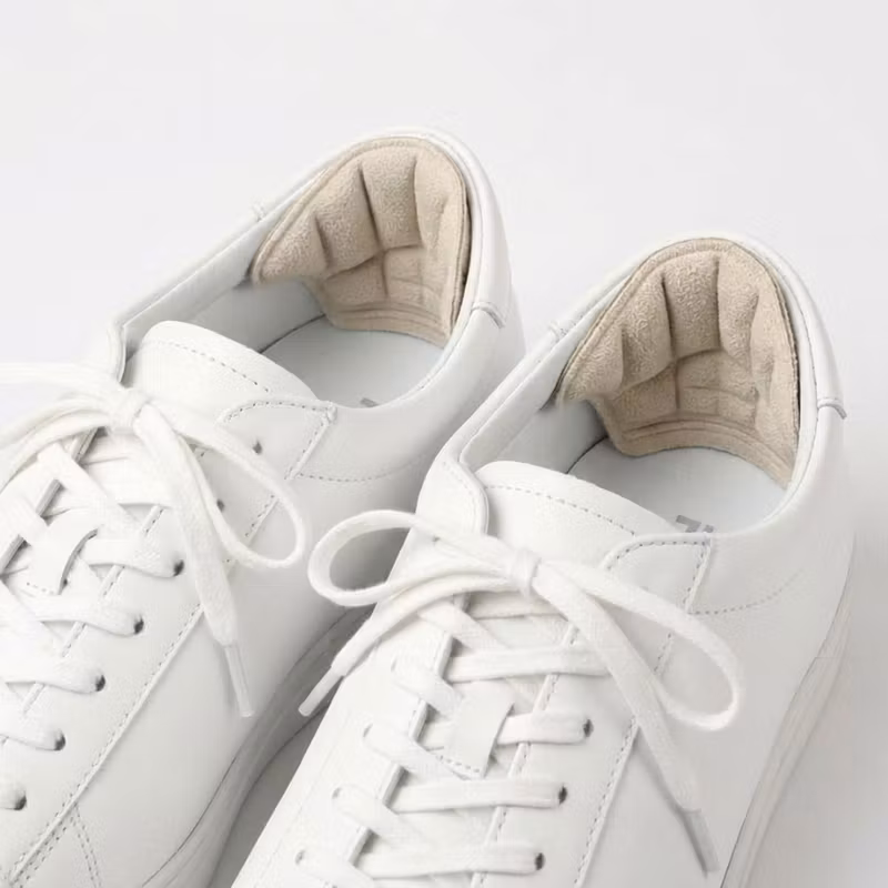 Beige hälgrepp monterade på insidan av hälpartiet i vita sneakers