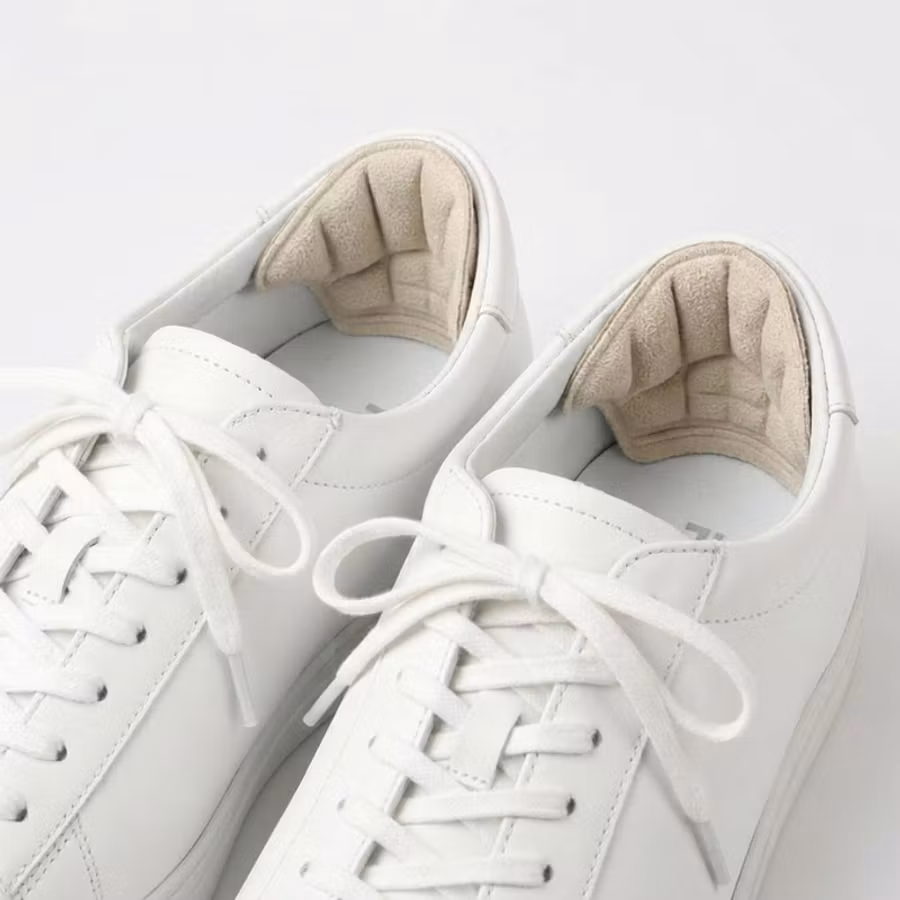 Beige hälgrepp monterade på insidan av hälpartiet i vita sneakers