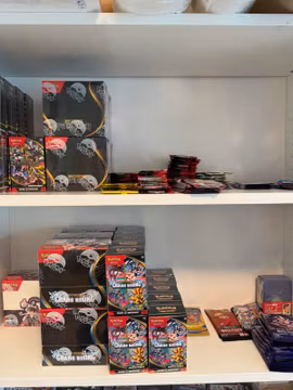 Två hyllplan med Pokémon-displaylådor, booster bundles och lösa boosterpaket.