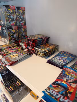 Sorterade högar med Pokémon-boosterpaket i engelsk och japansk utgåva på ett vitt hyllplan.